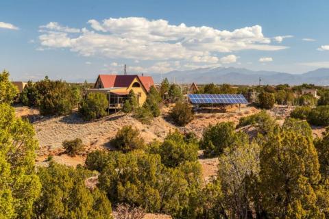 A rural residence with solar panels installed outdoors, set among desert vegetation with mountains in the distance.