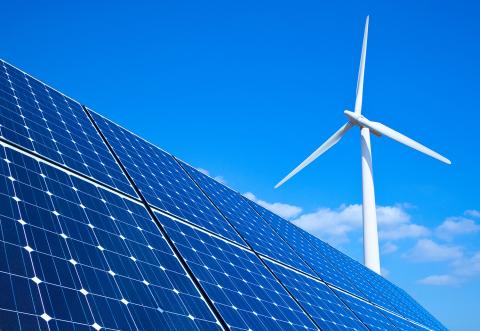 Solar panels cut across the foreground of an image featuring a blue sky and a white wind turbine