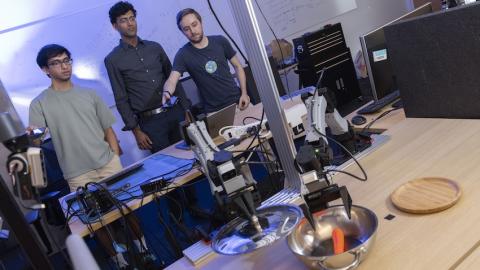 Three men use their phones to control a robot arm