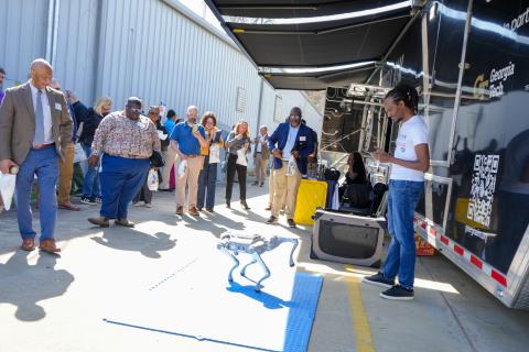 Group of educators gathered outside a Georgia Tech mobile lab watch a demonmanstration of a small four-legged robot during a campus outreach event.