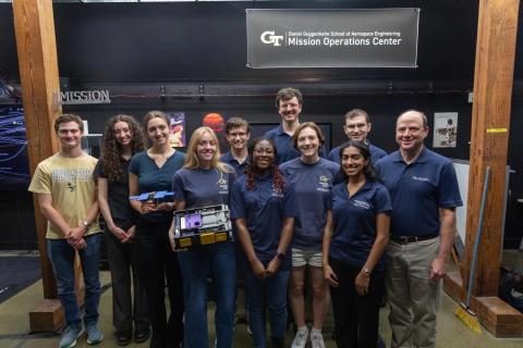 Georgia Tech students, faculty, and staff pose with spacecraft hardware beneath the Daniel Guggenheim School of Aerospace Engineering Mission Operations Center sign.