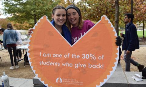 Two students hold a sign saying "I am one of the 30% of students who give back!"