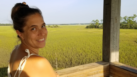 Kate Pride Brown smiling on a boardwalk in front of a green wetland area