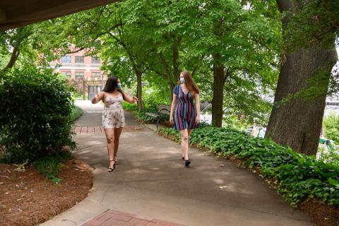 Two students walk around campus, several feet apart, with masks on.