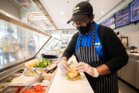 Photo of dining worker preparing a sandwich in a dining facility.