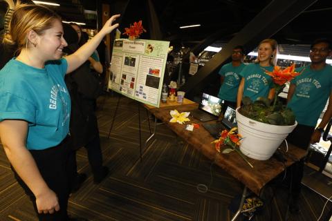 Student with arm in air standing in front of flower