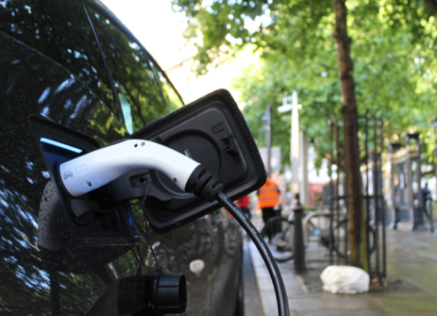 stock photo of an electric car plugged into a charger on the side of a road