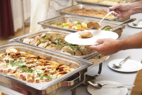 Person filling a plate at a buffet table. 