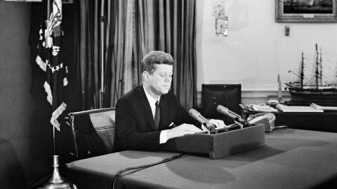 President John F. Kennedy (seated at desk) in front of two microphones to give a radio and television address to the nation on the Cuban Missile Crisis.