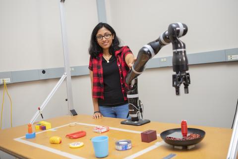 Lakshmi Nair stands next to a robotic arm with tool parts on a table