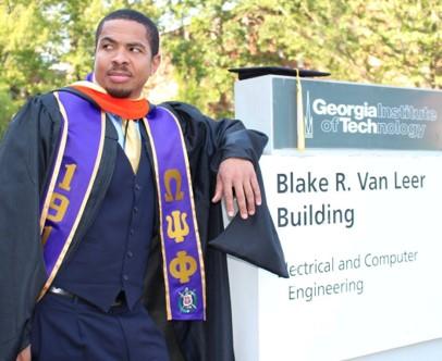 Joe Luck in cap and gown next to Van Leer signage