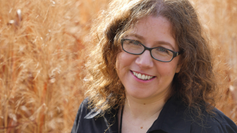 Photo of a woman wearing dark-rimmed glasses, curly brown hair, and a black shirt. 