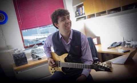 Matthew Gombolay smiles holding his guitar