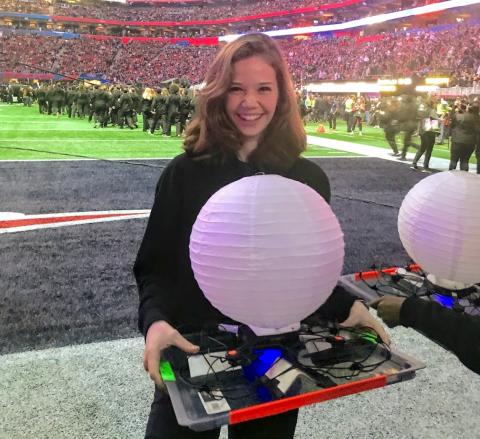 Georgia Tech CS Major Anna Klausen holding tray with lantern afixed to drone on Super Bowl LIII field