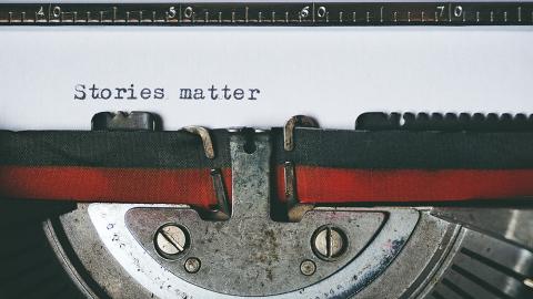 Closeup of a typewriter ribbon and a sheet of paper with the words "Stories matter." (Photo Courtesy: Suzy Hazelwood via Pexels)