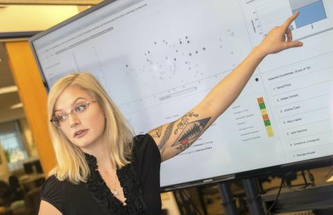 A female computer science student at Georgia Tech in front of and pointing to a whiteboard 