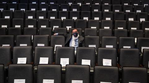 Aaron Shackelford, director of Georgia Tech Arts, wearing a mask, sitting alone in the Ferst Center for the Arts. Partially visible are the white pieces paper pinned to more than 700 of the seats to mark physically distanced seating.
