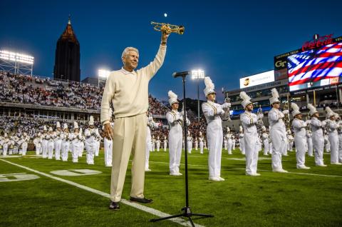 Image of Cecil Welch holding his trumpet on the field at Bobby Dodd in front of the marching band