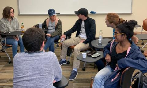 Several people sit in desks and talk as part of the German Club.