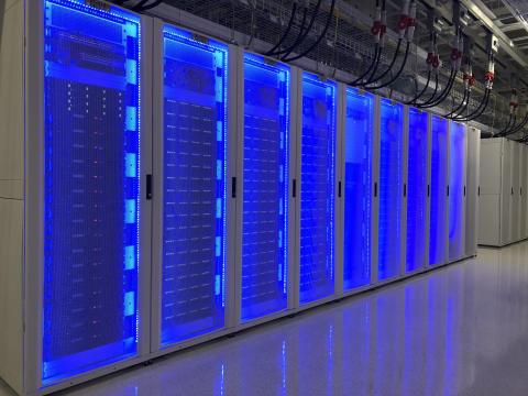 A row of computer servers illuminated with blue light in a white hallway.