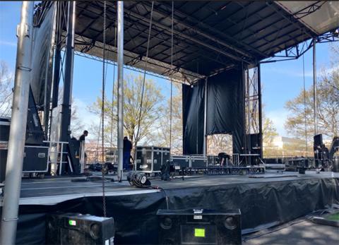 An outdoor stage, with metal truss framing it above and to the side. people are busy at work constructing it.