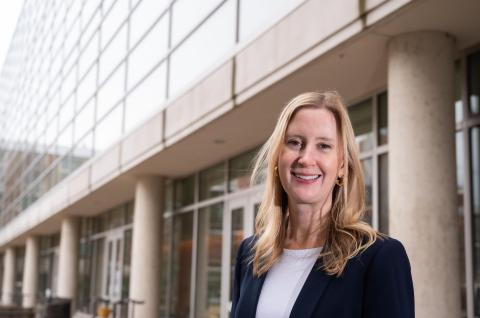 A headshot of Susan N. Thomas who is standing outside and smiling, wearing navy blue blazer over a white t-shirt. 