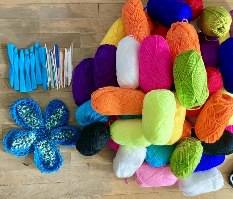 a handful of blue crochet hooks are lined up next to a tall colorful pile of skeins of yarn