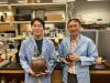 Two people wearing blue lab coats holding ancient earthenware pots that are hooked up with sensors. 