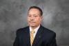 Dr. Archie W. Ervin is sitting in front of a grey and white marbled photo backdrop, wearing a white shirt, yellow striped tie, and a GT pin on his lapel. He has a monotone look on his face and is looking directly at the camera.