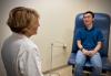 A female doctor speaks with a smiling male patient in an exam room