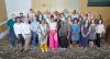 The seventh cohort of the Inclusive Leaders Academy and faculty/staff supporting members stand on patterned carpet, smiling.