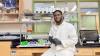 Augustine Atta Debrah, a second-year Chemistry Ph.D. student in Stockton’s Lab, sits in a white lab coat holding a sample.