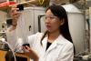 A woman with dark hair holds a glass tube filled with white fibers. 