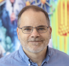 A white middle-aged man with brown/gray hair and glasses in front of a colorful, abstract background