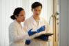 Two research scientists, a man and a woman, discuss their findings while standing in a lab wearing protective gear.