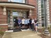 Eight students standing in front of a brick residence hall.