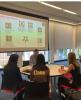 A man sitting in front of a screen talks with 3 students at a round table.