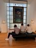 Three students sit in reflection in front of arts pieces at museum.