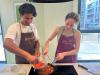 A young man strains tomatoes into a pan held by a young woman.