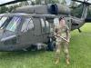 Mason Ladd stands in uniform holding an axe in front of a military helicopter.
