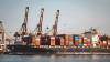 Large cargo ship docked at empty port with stacked containers and idle cranes