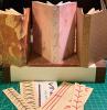 Three neutral colored books with creative bindings, stacked on a larger book that is flat underneath. Bookbinding sewing patterns displayed in front of books.