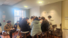 A group of middle and high school students at the NACLO Competition are gathered around a table in a classroom, working together and laughing.