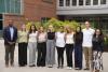 Ten people stand in a row in front of a building.