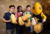 Three Georgia Tech students stand with Buzz, holding pompoms. The student in the middle is speaking into a microphone.