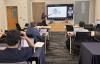 Image of classroom with woman pointing at a screen with full class in front of her.
