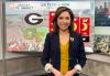 A woman with brown hair sits at a TV anchor desk with weather graphics behind her.