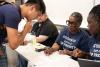 Two employees assist new student with onboarding documents and I-9 verification at event.