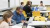 Students seated at tables look at their laptops during a class.