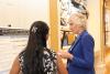 A student with long black hair stands in front of a research poster next to a woman with white hair in a blue suit.